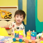 A little boy smiling at the camera while playing with toys