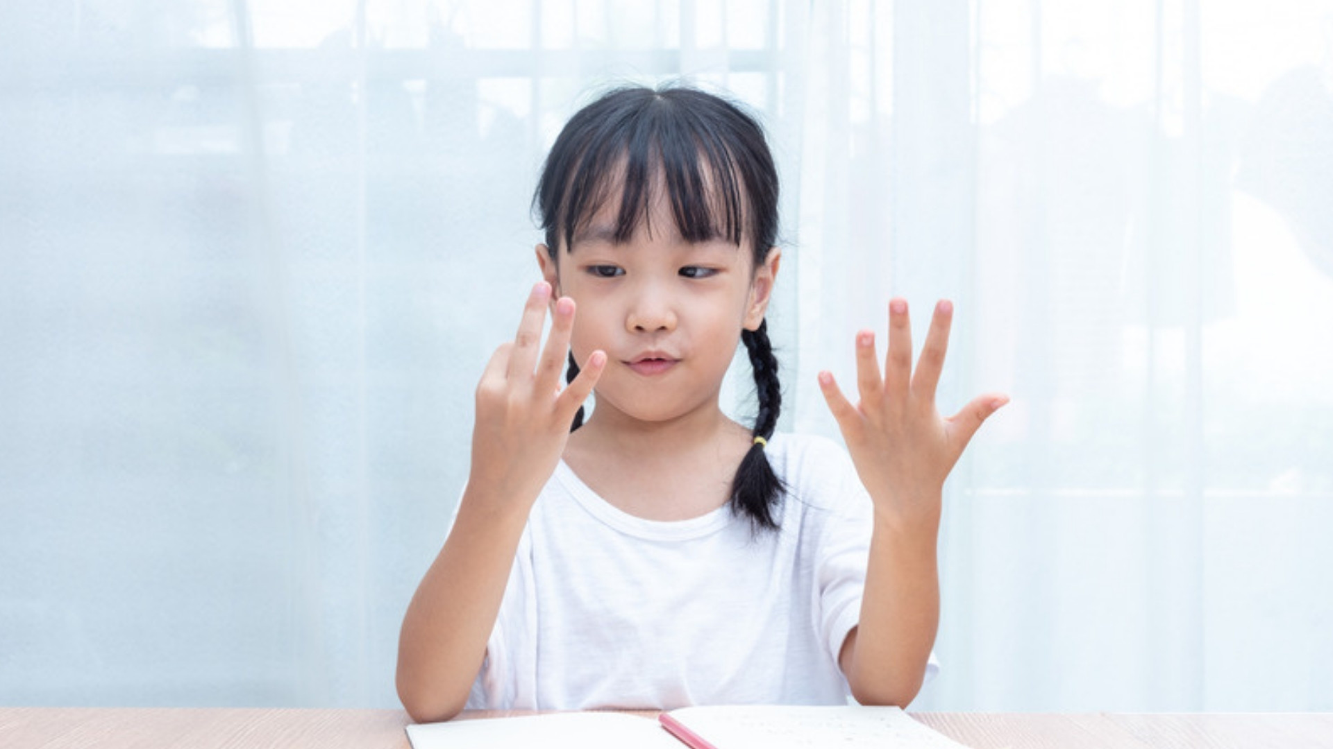 A young girl counting on her fingers at a table at home